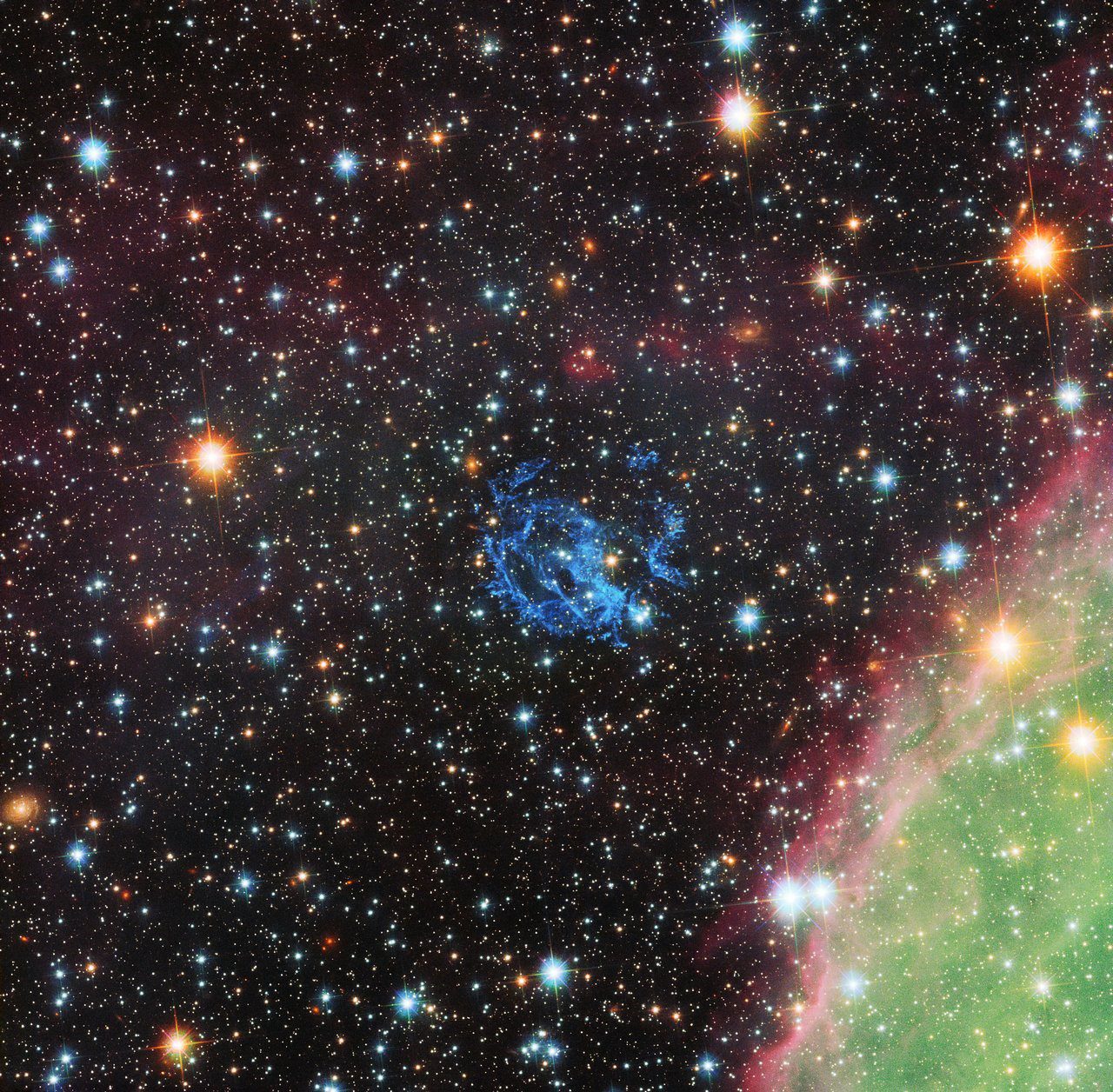 يظهر في هذه الصورة -التي التقطها تلسكوب هابل- تكوين بقايا السوبر نوفا (1E 0102.2-7219) من خيوط الغاز المرئية باللون الأزرق في منتصف الصورة. وأيضًا يمكننا رؤية منطقة تكوين النجم الضخم N76 باللونَيْن الأخضر والزهري في أسفل يمين الصورة. 